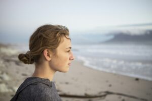 Profile portrait of a teenage girl looking out to sea from a beach at sunset.